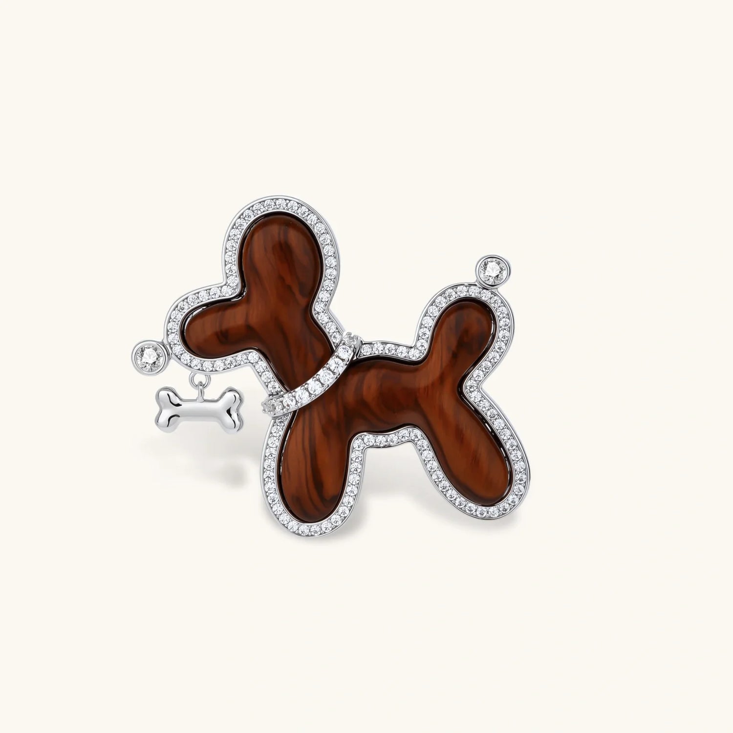 Dog-shaped brooch with copper base, palladium plating, crystal accents, and dangling bone charm against cream background