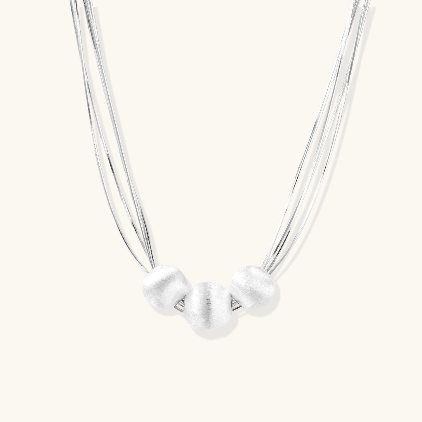 Sterling silver multi-strand necklace with three brushed round beads on cream background