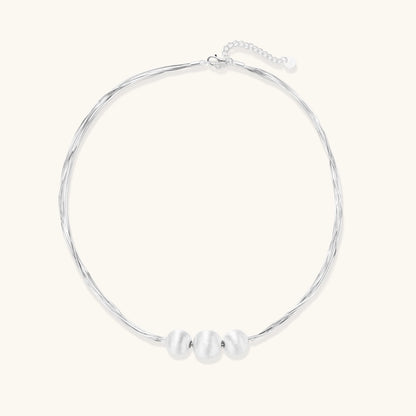Sterling silver multi-strand necklace with three brushed round beads on cream background