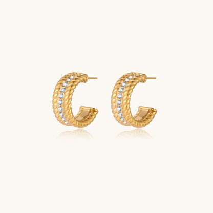 Textured gold huggie hoop earrings with raised ribbed rows creating dimensional sculptural design on cream background