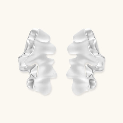 Pair of silver-toned sculptural earrings with flowing abstract forms and stud backs against white background.