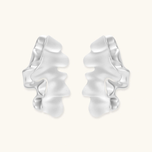 Pair of silver-toned sculptural earrings with flowing abstract forms and stud backs against white background.