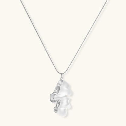 Modern sculptural pendant necklace with twisted metallic design on delicate silver chain against neutral background.