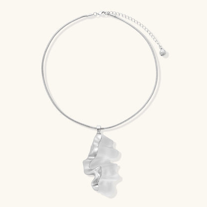 Modern sculptural pendant necklace with twisted metallic design on delicate silver chain against neutral background.