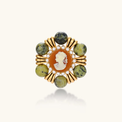 Ornate gold-plated brooch with central cameo, radiating spokes, pearl border, and green marbled natural stones on white background.