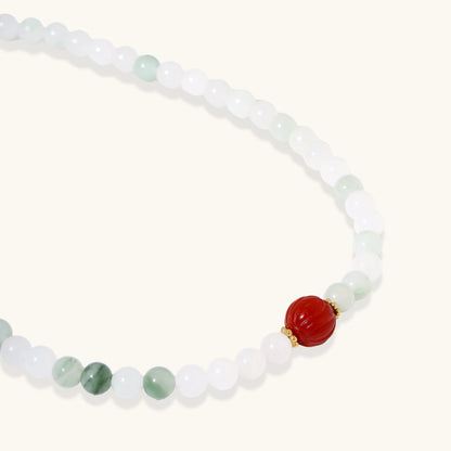 Three layered white beaded bracelets with carved orange agate lotus centerpiece and freshwater pearls on cream background.