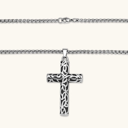 Silver stainless steel Celtic cross pendant with filigree vine pattern on a box chain, against a cream background.