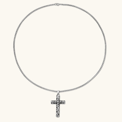 Silver stainless steel Celtic cross pendant with filigree vine pattern on a box chain, against a cream background.